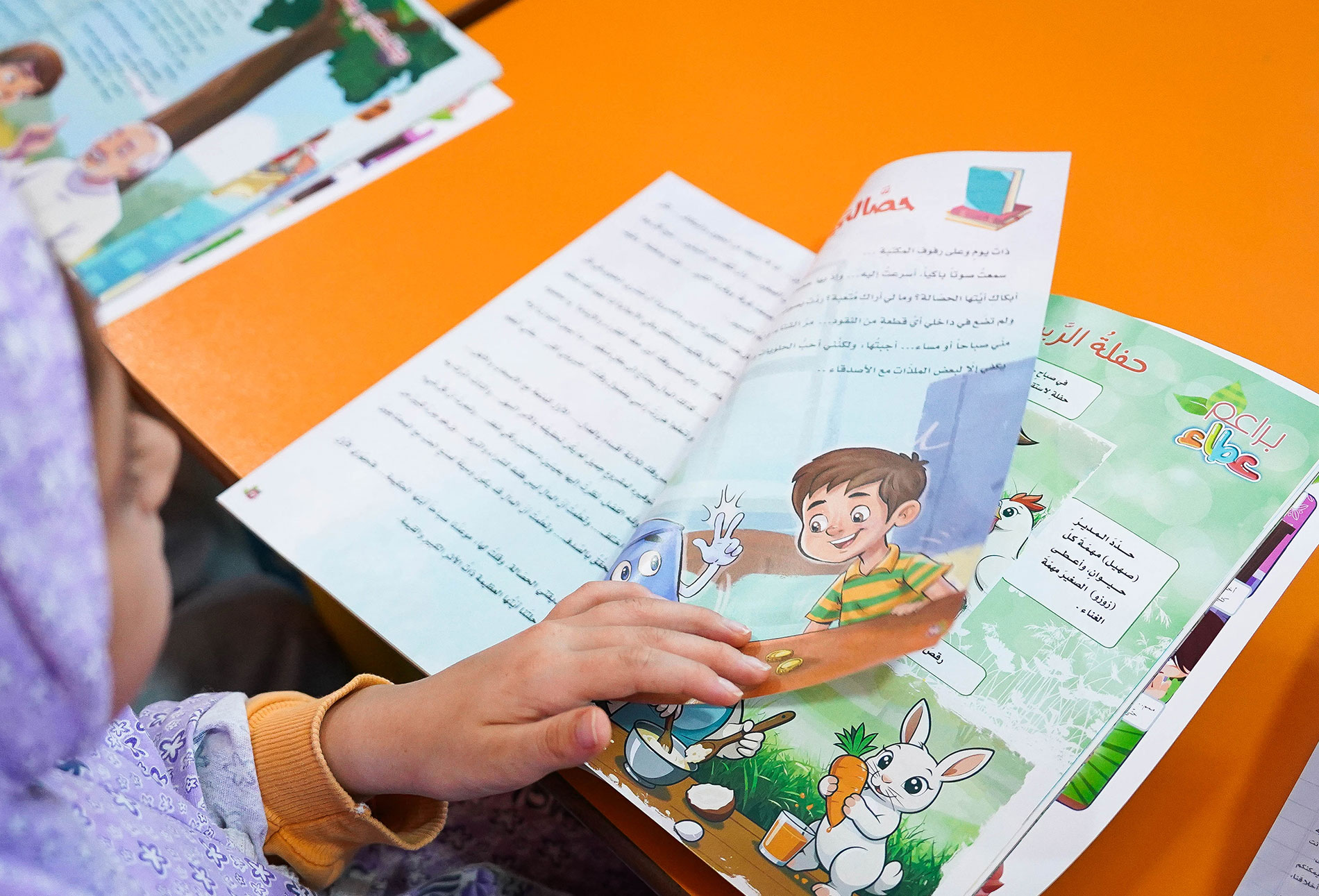 طالبة تجلس في مقعدها داخل أحد صفوف المدرسة وتقرأ مجلة عطاء