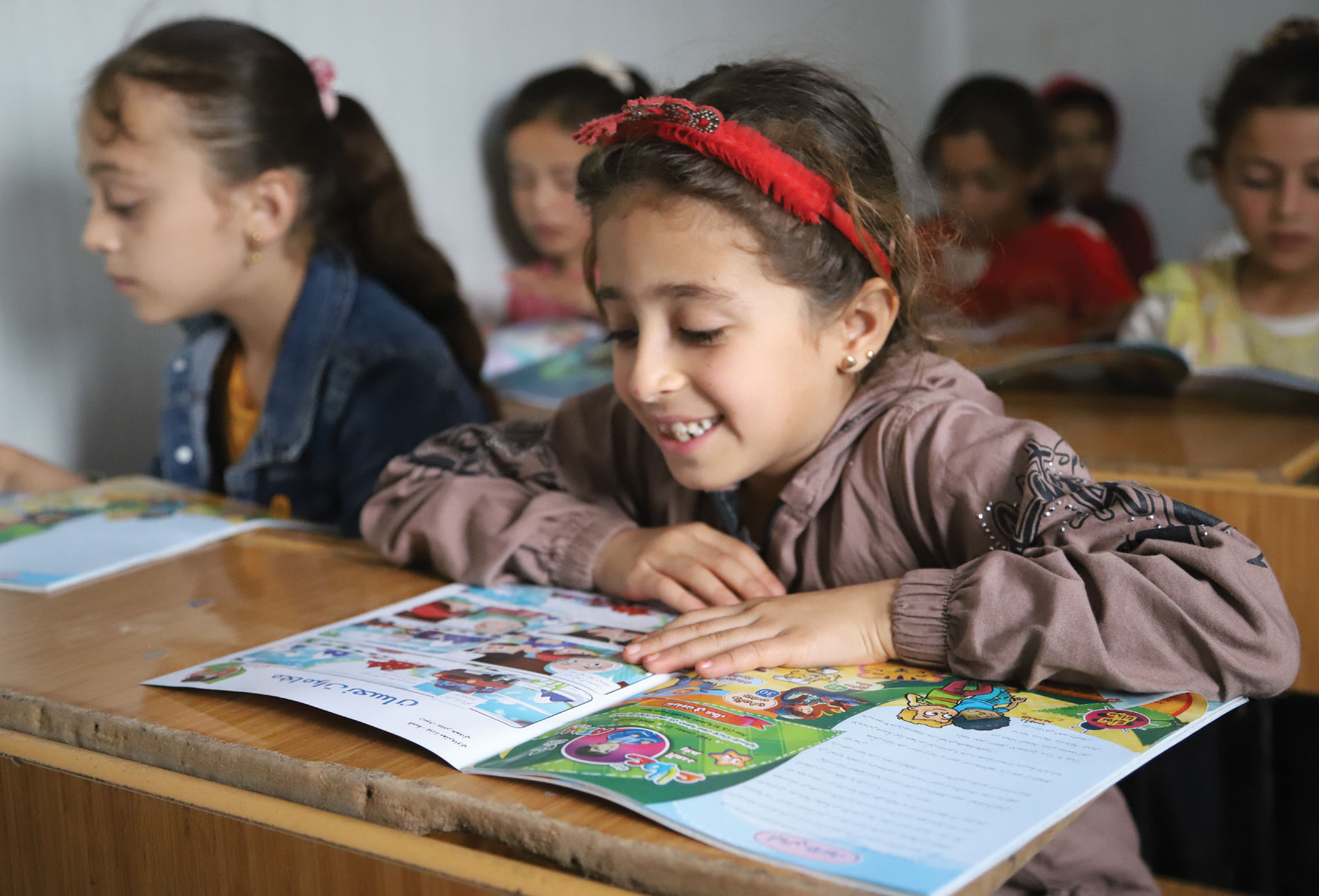 طالبة تجلس في مقعدها داخل أحد صفوف المدرسة وتقرأ مجلة عطاء